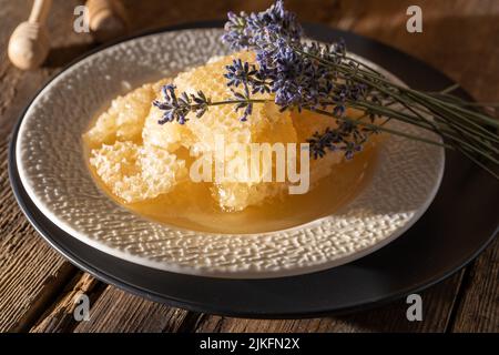 Honig und Waben auf einem weißen Teller. Süßes Essen in einer Schüssel auf dem Tisch. Ein Produkt der Imkerei. Lavendelblüte. Stockfoto