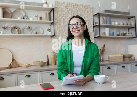 Lächelnde Brünette, die im Heimbüro steht und die Kamera anschaut Stockfoto