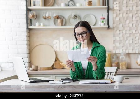 Seriöse und fokussierte Geschäftsfrau freiberuflich auf Papier arbeiten zu Hause in der Küche, brünett in der Brille und grün in der Küche, zahlen und Rechnungen zu berechnen Stockfoto