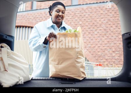 Waist up Porträt der schwarzen Frau Putting Lebensmittel in Kofferraum auf dem Parkplatz Stockfoto