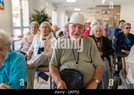 Senioren, die auf Stühlen oder Rollstühlen sitzen und ein Musikkonzert in einem Altersheim besuchen. Stockfoto