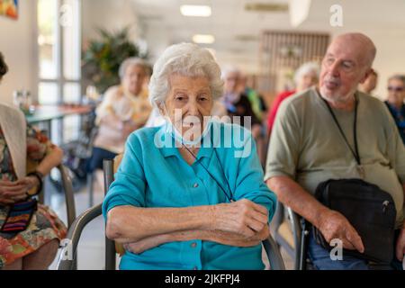 Senioren, die auf Stühlen oder Rollstühlen sitzen und ein Musikkonzert in einem Altersheim besuchen. Stockfoto