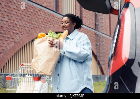 Porträt einer lächelnden Frau, die nach dem Einkaufen im Supermarkt eine Einkaufstasche in den Kofferraum legte Stockfoto