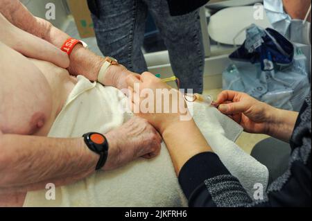 Private Krankenschwester, die während der Toilette einen Bluttest und eine Insulinininjektion an einem 87-jährigen Patienten durchführt. Die Patientin ist mit einem Armband für Fernalarm am Handgelenk ausgestattet. Stockfoto