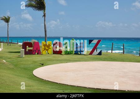 Cancun, Quintana Roo, Mexiko - 24. April 2022: Cancun farbenfrohes Schild am blauen Ozean in der Karibik. Blick mit grünem Gras und Palmen. Touristenort Stockfoto