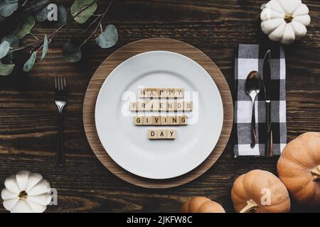 Thanksgiving Platz Einstellung mit Teller, Serviette, auf einem dekorierten Tisch aus flacher Lage oder Draufsicht Position geschossen. Happy Friendsgiving Day wurde geschrieben. Stockfoto