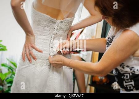 Brautjungfern helfen der Braut, ihr Hochzeitskleid anzuziehen Stockfoto