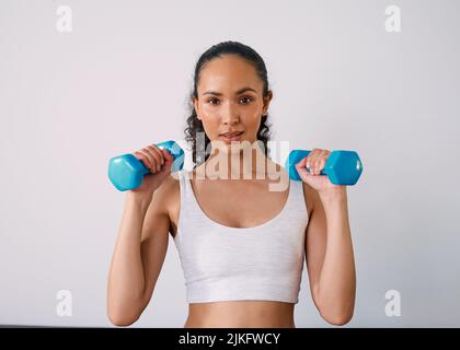 Eine ernsthafte junge Frau hebt kleine Gewichte, um zu Hause stark zu werden Stockfoto