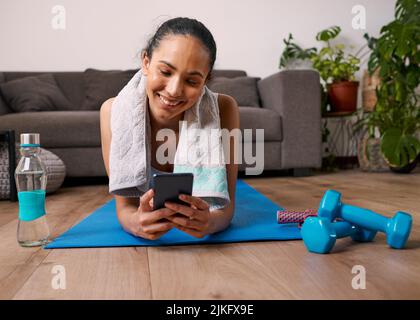 Eine junge, multiethnische Frau verfolgt ihre Übungen nach dem Training in der Fitness-App Stockfoto