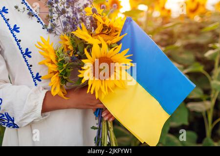 Frau mit gelber und blauer Flagge der Ukraine mit Sonnenblumen im Sommerfeld. Unabhängigkeitstag der Ukraine. Nahaufnahme Stockfoto