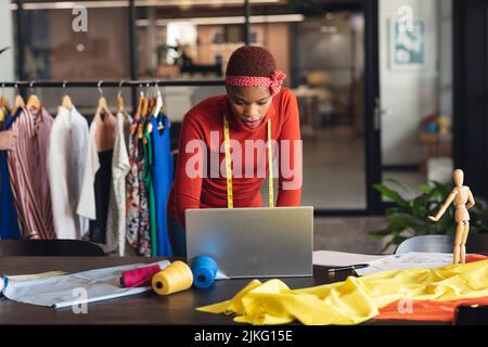 afroamerikanische Modedesignerin, die am Schreibtisch im Studiobüro am Laptop arbeitet Stockfoto