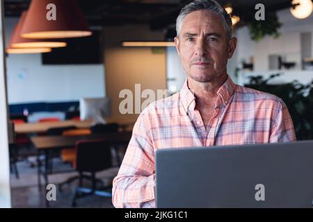 Porträt eines ernsthaften kaukasischen reifen Geschäftsmannes mit Laptop im kreativen Büro Stockfoto