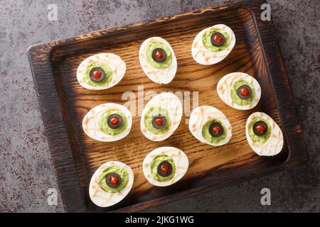 Köstliche deviled Eier gefüllt mit Guacamole und Oliven close-up auf einem Holztablett auf dem Tisch. Horizontale Ansicht von oben Stockfoto