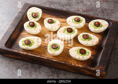 Monster Eyes deviled Eier mit einer Avocado und Oliven für den Halloween-Tag auf einem Holztablett auf dem Tisch. Horizontal Stockfoto