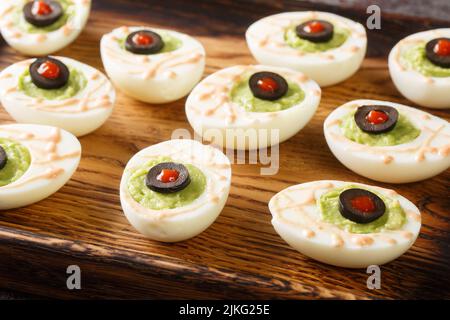 Lustige Halloween-Lebensmittel Augäpfel deviled Eier gefüllt mit Avocado-Creme auf einem Holztablett auf dem Tisch. Horizontal Stockfoto