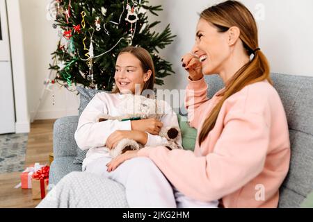 Weiße Mutter und Tochter lachen und reden, während sie sich zu Hause auf dem Sofa ausruhen Stockfoto