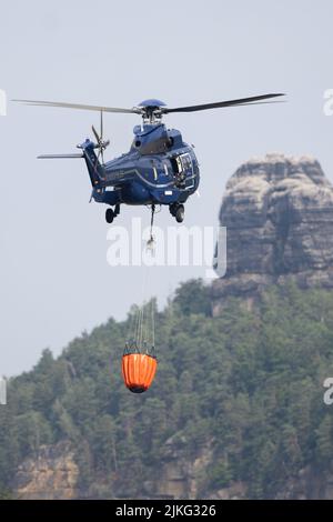 Schmilka, Deutschland. 02. August 2022. Ein Hubschrauber holt mit einem externen Wasserbehälter Wasser aus der Elbe, um einen Waldbrand im Nationalpark Sächsische Schweiz zu löschen. Quelle: Sebastian Kahnert/dpa/Alamy Live News Stockfoto