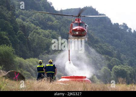 Schmilka, Deutschland. 02. August 2022. Ein Hubschrauber fliegt über ein Feuerwasserbecken, um Wasser zu sammeln und einen Waldbrand im Nationalpark Sächsische Schweiz zu löschen. Quelle: Sebastian Kahnert/dpa/Alamy Live News Stockfoto