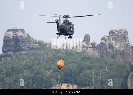 Schmilka, Deutschland. 02. August 2022. Ein Hubschrauber fliegt über ein Feuerwasserbecken, um Wasser zu sammeln und einen Waldbrand im Nationalpark Sächsische Schweiz zu löschen. Quelle: Sebastian Kahnert/dpa/Alamy Live News Stockfoto