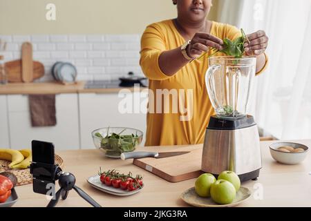 Ein kurzer Schuss schwarzer Frau, die Spinat in den Mixer setzt, während sie zu Hause einen gesunden Smoothie macht, Platz kopieren Stockfoto