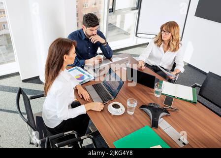 Man hat einen Blick auf Geschäftsfrauen und Geschäftsleute, die am Schreibtisch sitzen und einen Laptop benutzen, während sie eine Tagung in einem Konferenzraum abhalten. Stockfoto