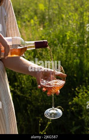 Frau gießt Rosenwein inro ein Glas in einem Sommergarten Stockfoto