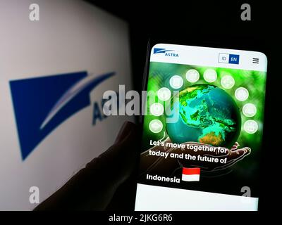 Person hält Handy mit Website der indonesischen Firma PT Astra International Tbk auf dem Bildschirm mit Logo. Konzentrieren Sie sich auf die Mitte des Telefondisplays. Stockfoto