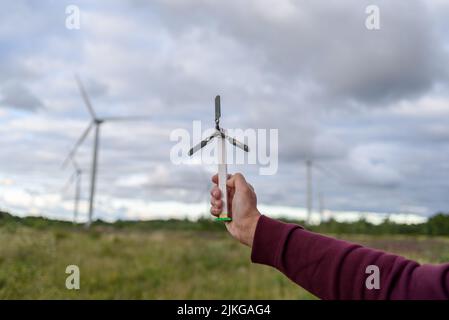 Spielzeug Windkraft Turbine aus Kindern Baukasten Blöcke halten in der Hand mit echten Turbinen auf dem Hintergrund. Grüne erneuerbare Energien Stockfoto