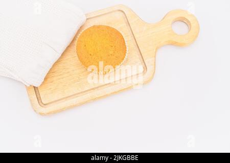 Karottenkuchen aus biologischem Anbau in einem Papierbecher mit Dinkelmehl, Küchentuch und Holzschneidebrett auf einem weißen Tisch Stockfoto