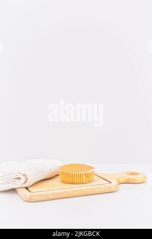 Karottenkuchen aus biologischem Anbau in einem Papierbecher mit Dinkelmehl, Küchentuch und Holzschneidebrett auf einem weißen Tisch Stockfoto