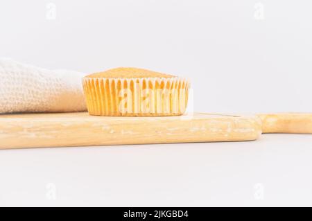 Karottenkuchen aus biologischem Anbau in einem Papierbecher mit Dinkelmehl, Küchentuch und Holzschneidebrett auf einem weißen Tisch Stockfoto