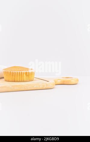 Karottenkuchen aus biologischem Anbau in einem Papierbecher mit Dinkelmehl, Küchentuch und Holzschneidebrett auf einem weißen Tisch Stockfoto