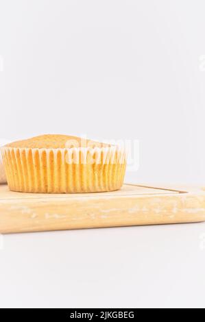 Karottenkuchen aus biologischem Anbau in einem Papierbecher mit Dinkelmehl, Küchentuch und Holzschneidebrett auf einem weißen Tisch Stockfoto