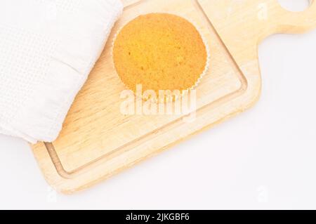 Karottenkuchen aus biologischem Anbau in einem Papierbecher mit Dinkelmehl, Küchentuch und Holzschneidebrett auf einem weißen Tisch Stockfoto