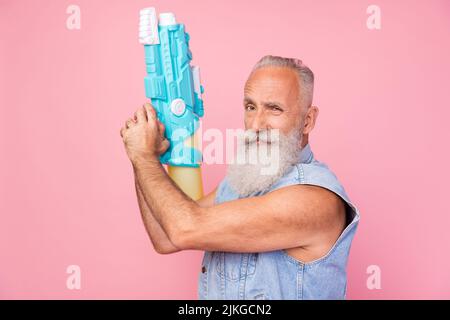 Foto von charmanten coolen Mann Rentner gekleidet Denim Weste steigenden Wasserpistole suchen Sie isoliert rosa Farbe Hintergrund Stockfoto