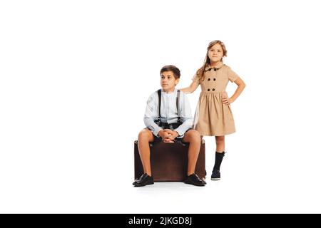 Porträt von stilvollen Kindern in Retro-Stil Outfits posieren, sitzen auf Retro-Koffer isoliert über weißen Studio-Hintergrund. Reisen Stockfoto