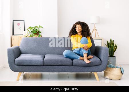 Entspannt lächelnde afroamerikanische Frau, die zu Hause auf dem Sofa sitzt Stockfoto