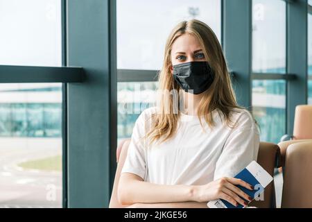 Biometrischer ukrainischer Pass in den Händen einer Frau, die am Flughafen in die Kamera schaut. Bürger der Ukraine ist gezwungen, ihr Zuhause wegen des Krieges mit zu verlassen Stockfoto