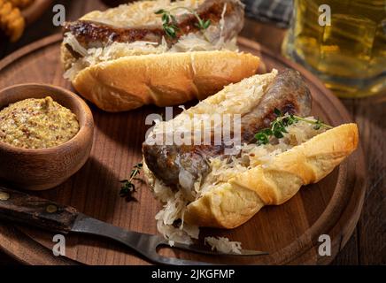 Gegrillte Bratwurst und Sauerkraut auf einem Brötchen mit Senf in einer Schüssel auf einer Holzplatte Stockfoto