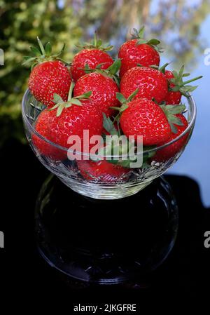 Glasschale mit frischen roten Erdbeeren im Sommer auf einem Tisch im Garten. Stockfoto