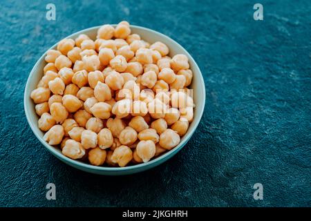 Nahaufnahme einer Keramikschale mit einigen gekochten Kichererbsen, auf einer dunklen Steinoberfläche Stockfoto