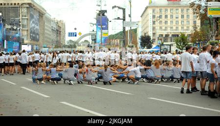 Eine Gruppe junger Mädchen in Seemannswesten, die auf Asphalt sitzen und vor dem Flash Mob Figuren wiederholen, andere Gruppen in weißen Kostümen, die auf der Straße stehen Stockfoto