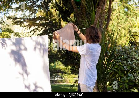 Junger, nicht erkennbarer Mann von hinten, der im Sommer mit Schatten die Wäsche im heimischen Garten hinauhängt Stockfoto