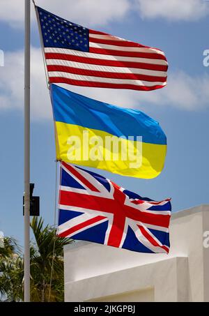 Flaggen von drei Nationen, den Vereinigten Staaten, der Ukraine und dem Vereinigten Königreich, auf weißem Fahnenmast Stockfoto