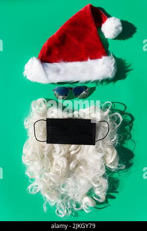 weihnachtsmann mit Sonnenbrille in schützender covid-19 Gesichtsmaske auf grünem Hintergrund Stockfoto
