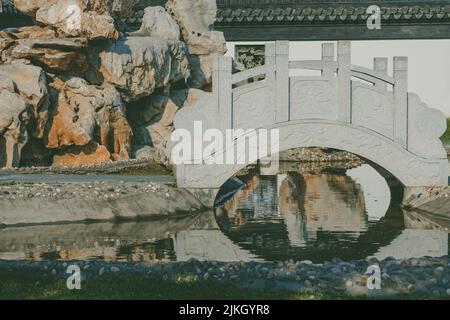 Eine kleine Bogenbrücke auf einem Fluss mit großen Felsen und Reflexion im Wasser Stockfoto