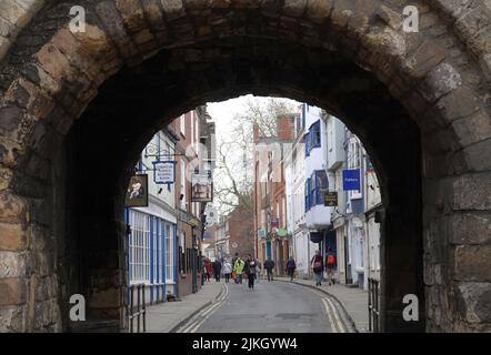 Eine Gruppe von Menschen, die auf der Straße durch den Torbogen der Bootham Bar in York, Großbritannien, spazieren Stockfoto