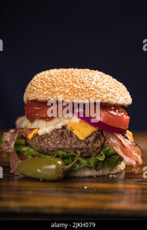 Ein Sandwich mit Käse-Burger mit Salat, Zwiebeln, Pfeffer und Tomaten auf einem Holztisch Stockfoto