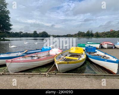 Eine Reihe von farbenfrohen Ruderbooten, die auf der Meare in Thorpeness, Suffolk, Großbritannien, gemietet werden können Stockfoto