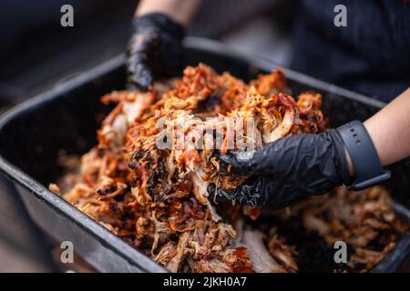 Die Hände eines Küchenchefs mischen Fleisch mit Sauce in einem schwarzen Stockfoto